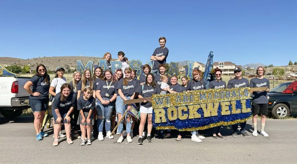 Un gruppo di giovani posa davanti a uno striscione della Rockwell Charter School con un paesaggio montano sullo sfondo.