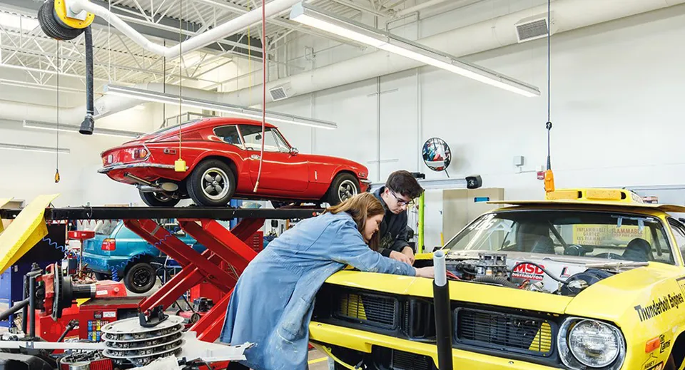 Uno studente lavora su un'auto d'epoca rossa sul ponte sollevatore nell'officina della Centennial Secondary School in Ontario.