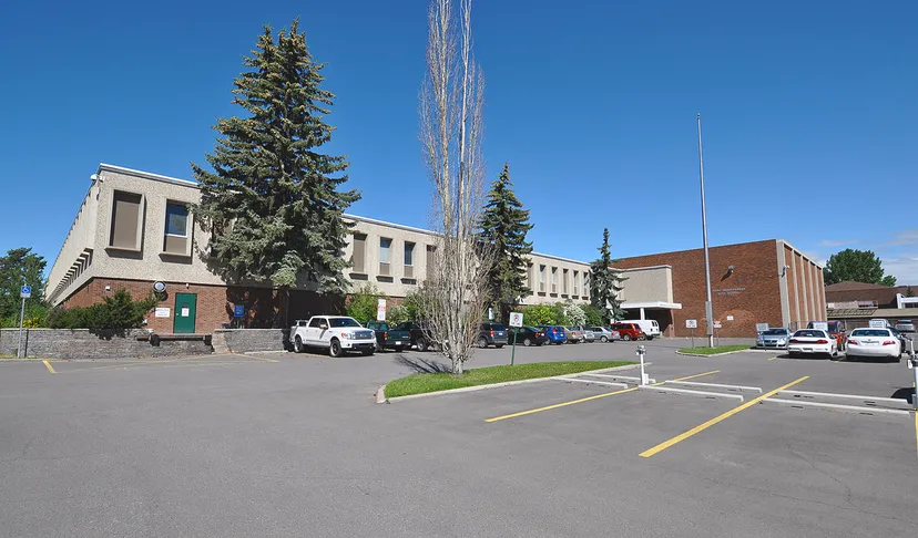 L'edificio in mattoni a più piani della Lord Beaverbrook High School con un grande albero sempreverde in primo piano sotto un cielo limpido.
