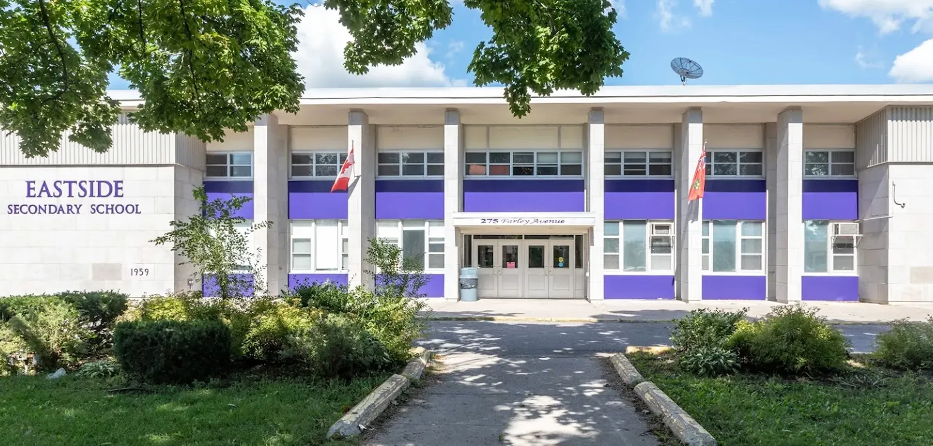 L'edificio scolastico moderno a due piani della Eastside Secondary School è circondato da aree verdi e da un vialetto pavimentato.