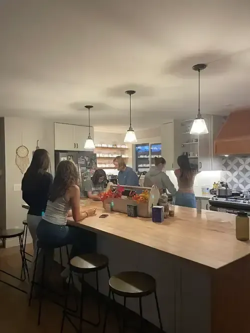 Grupo de alumnas charlando por la noche alrededor de la isla de una cocina familiar