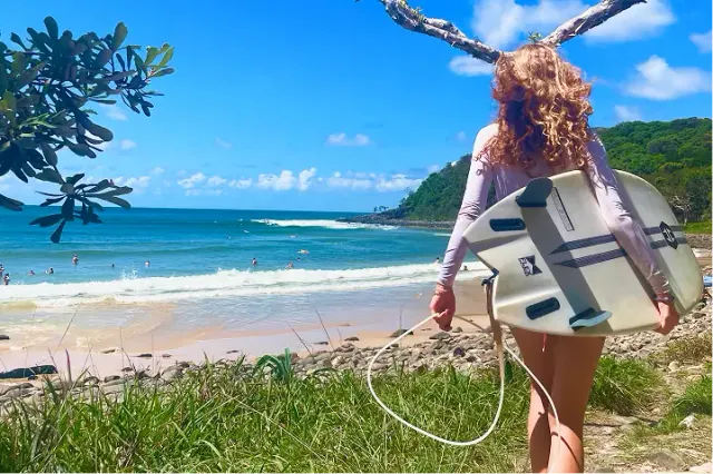 Ragazza con tavola da surf cammina verso una spiaggia oceanica in Australia