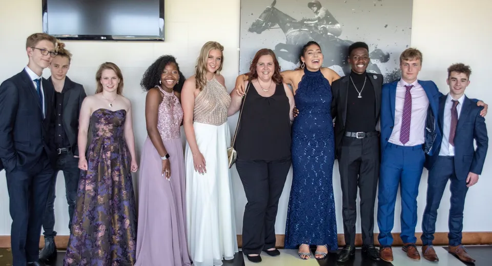 Un gruppo di persone in abbigliamento formale si trova davanti a una parete decorata nel complesso della Bredon School.