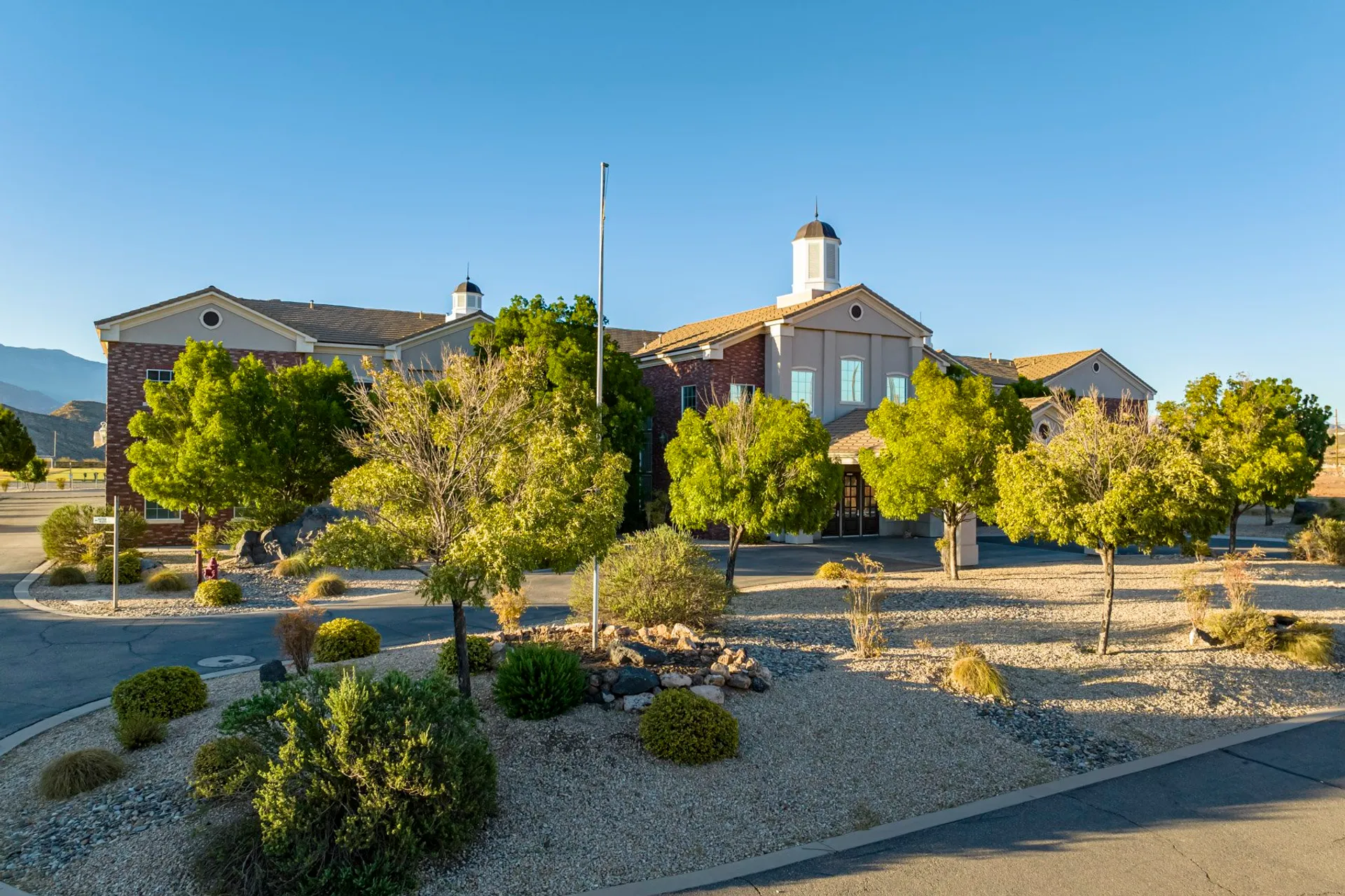 Area verde con arbusti e alberi ben curati nel campus della Utah Prep Academy sotto un cielo terso.