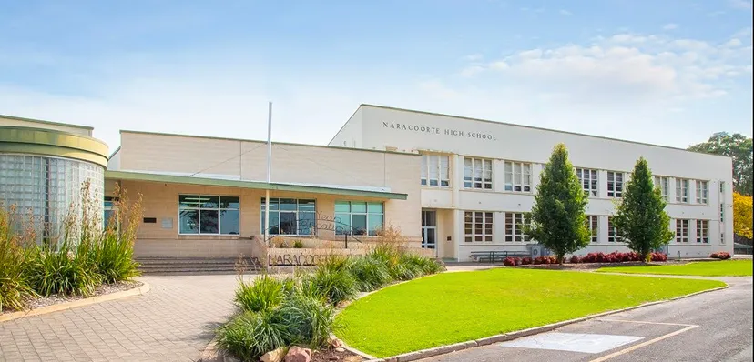 L'edificio scolastico moderno a più piani della Naracoorte High School con un prato ben curato e piante in primo piano sotto un cielo blu.