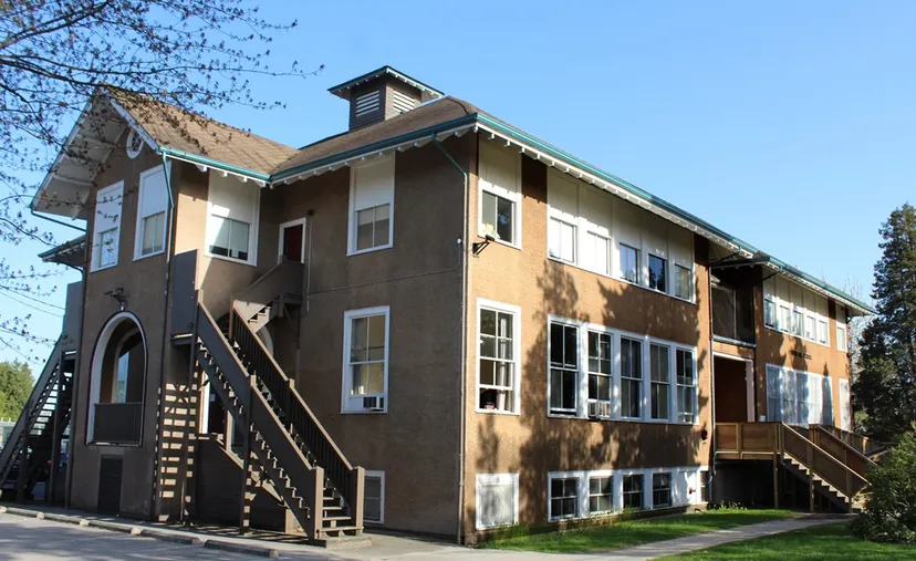 L'edificio residenziale a più piani con facciata in legno nel campus del South Hill Education Centre, circondato da alberi e aree verdi sotto un cielo blu.