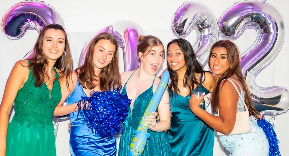 Cinque studentesse in abiti colorati mettono in posa davanti a grandi palloncini del numero 21 viola e argento nel campus della St. Catherine's School.