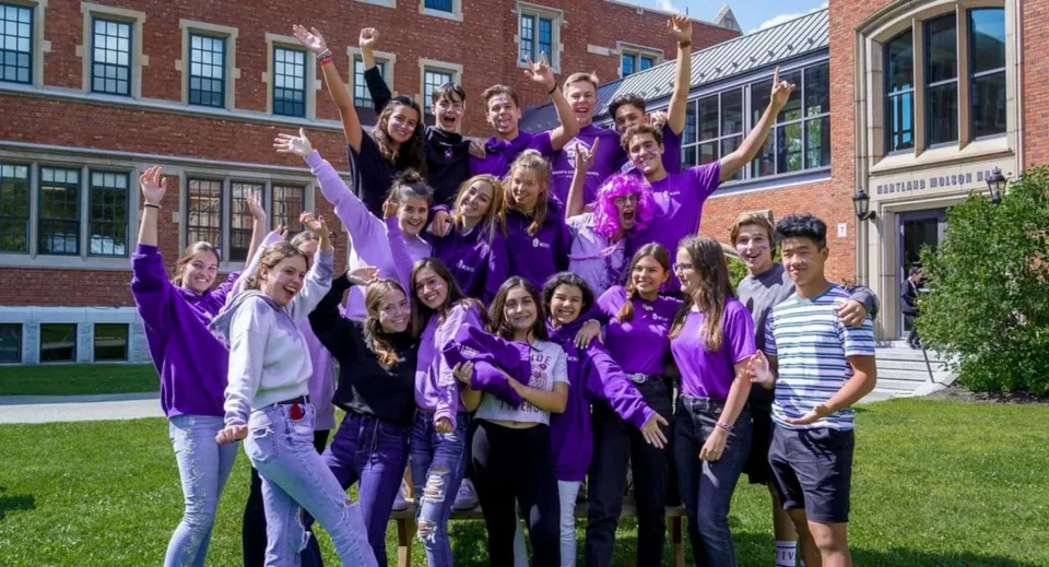 Un gruppo di studenti e studentesse in abiti viola posa davanti a un edificio in mattoni all'interno del campus della Bishop’s College School.