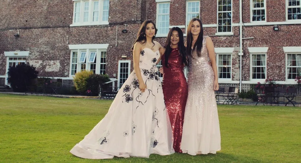 Tre studentesse della Rossall School in abito formale di fronte a un edificio in mattoni con ampie finestre e un prato.