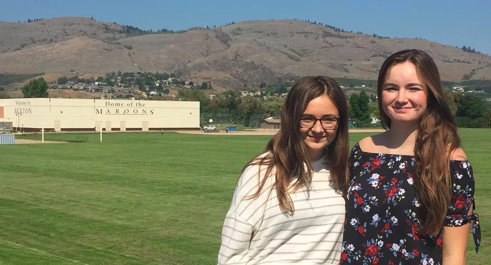 Due studentesse si trovano su un campo erboso con vista sulle montagne nel terreno della Clarence Fulton Secondary School.