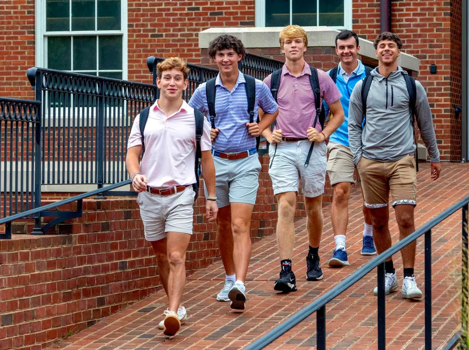Un gruppo di studenti della Woodberry Forest School cammina insieme su un viale lastricato davanti a un edificio con grandi finestre.