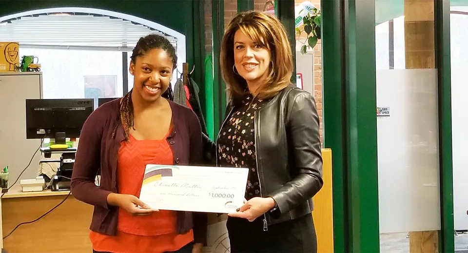 Due studentesse tengono insieme un certificato al Centre High Campus davanti a una parete verde con oggetti da esposizione.