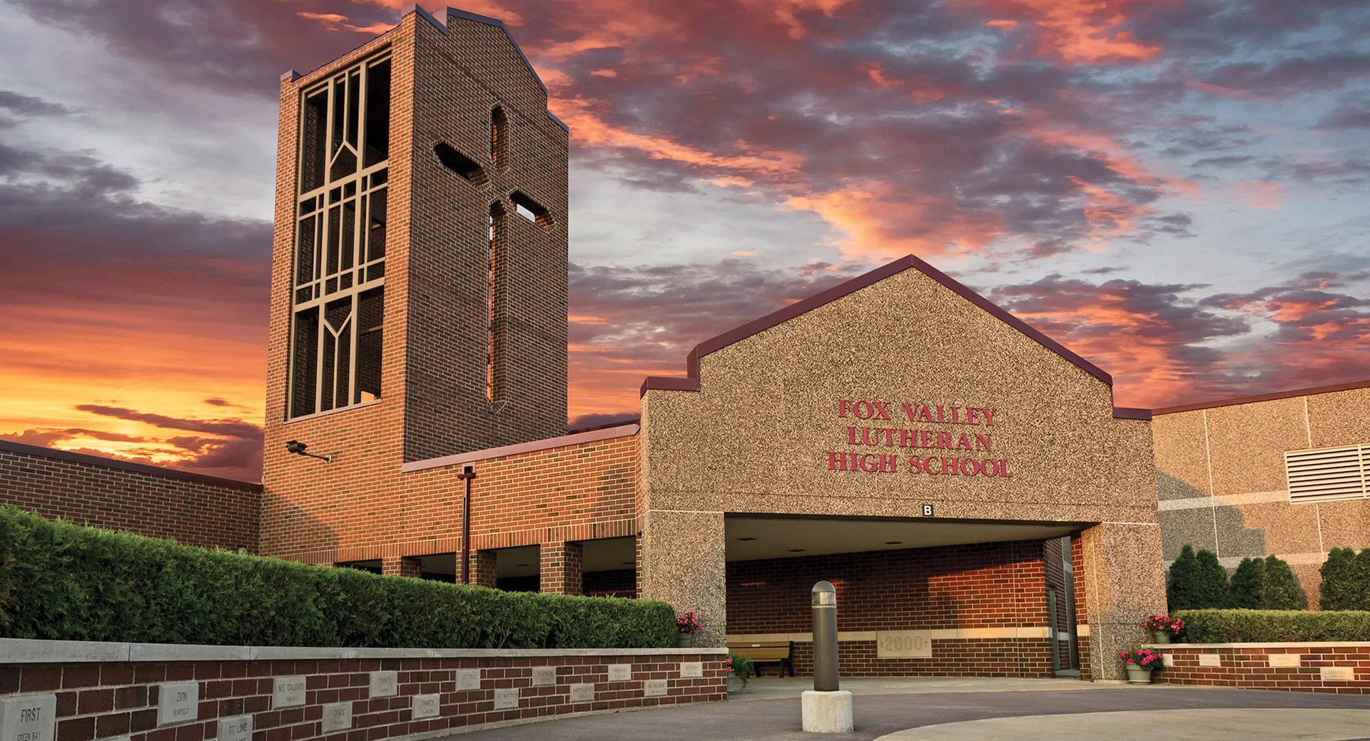 L'edificio in mattoni con un'alta torre della Fox Valley Lutheran High School si erge davanti a un cielo rosso intenso ed è circondato da aree verdi.