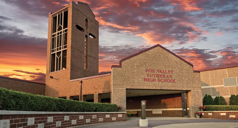 L'edificio in mattoni con un'alta torre della Fox Valley Lutheran High School si erge davanti a un cielo rosso intenso ed è circondato da aree verdi.