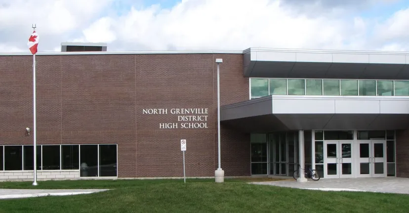 Il grande edificio in mattoni della North Grenville District High School si vede davanti a un cielo nuvoloso e a un prato.