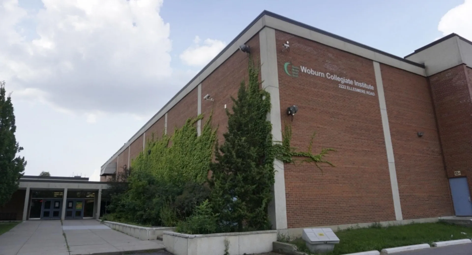 L'edificio del Woburn Collegiate Institute è circondato da una verde vegetazione e si staglia sotto un cielo limpido.