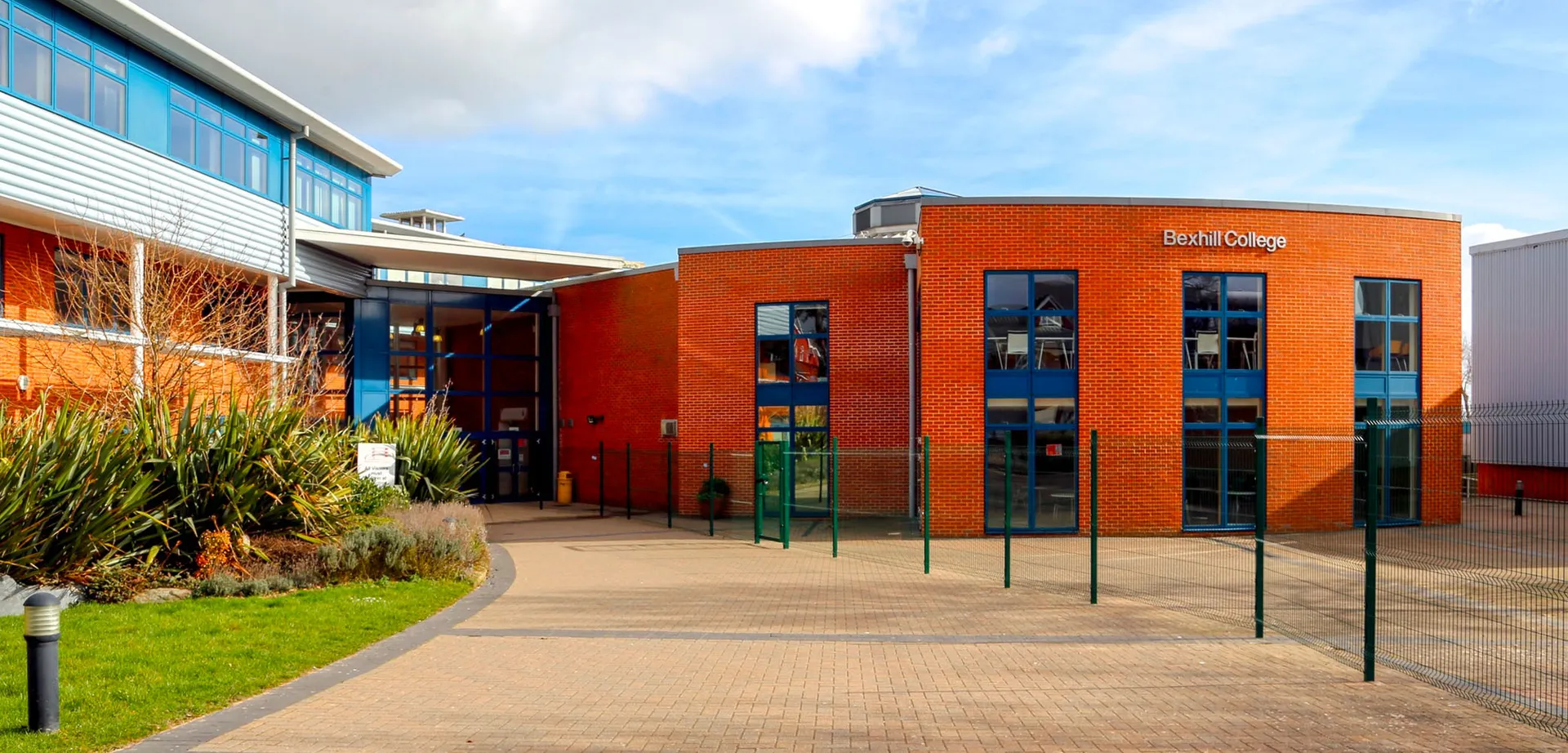 L'edificio moderno in mattoni del Bexhill College con grandi finestre e un viale verso l'ingresso circondato da aree verdi.