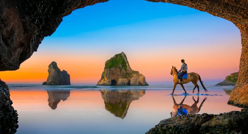 Una persona a cavallo sta sulla spiaggia davanti a delle rocce durante il tramonto vicino all'Alfriston College.
