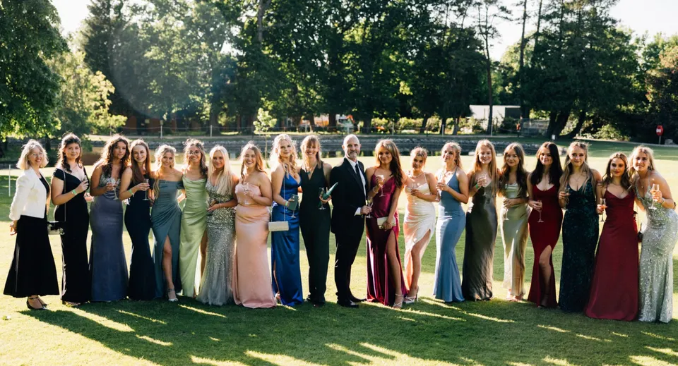 Un gruppo prevalentemente di giovani studentesse della Bede's Senior School insieme su un prato con alberi sullo sfondo.