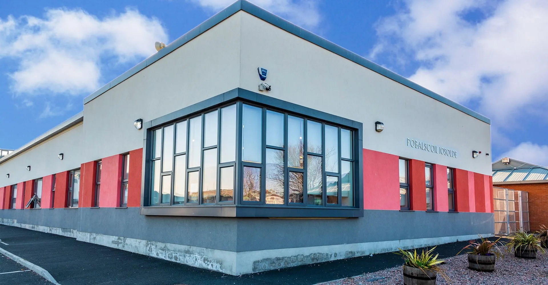 L'edificio moderno della Palmerstown Community School con grandi vetrate davanti a un cielo blu e nuvole bianche.