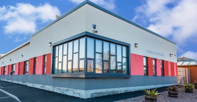 L'edificio moderno della Palmerstown Community School con grandi vetrate davanti a un cielo blu e nuvole bianche.