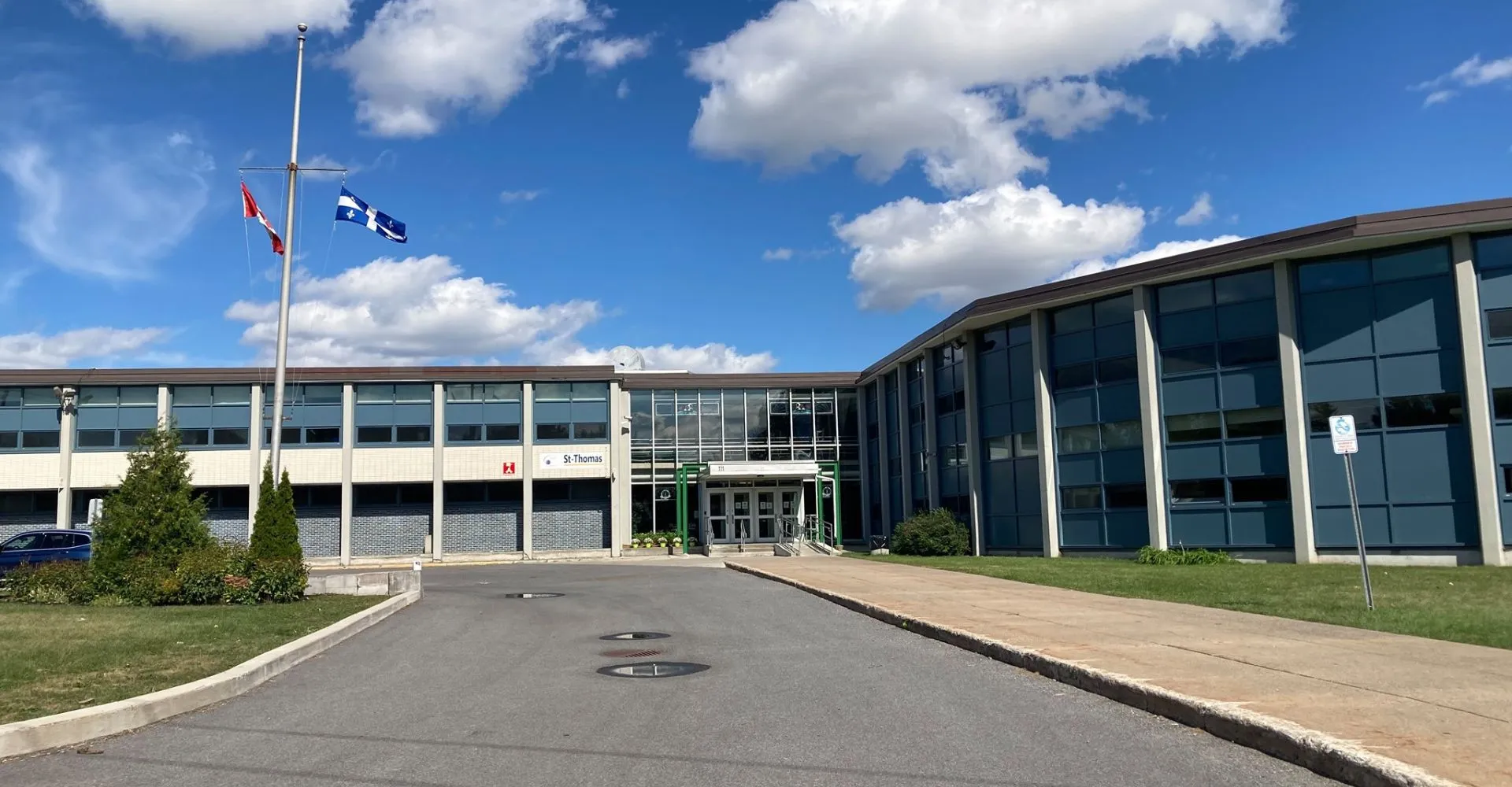 L'edificio moderno a più piani della St. Thomas High School con pareti in vetro e viale d'accesso pavimentato sotto un cielo blu.