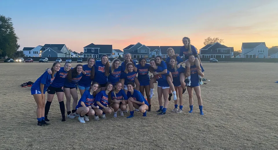 Un gruppo di giovani atlete della Bootham School posa insieme su un campo in erba al tramonto.