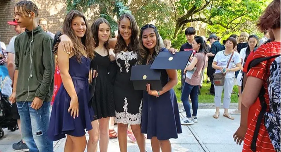 Un gruppo di giovani diplomate sta all'aperto nel campus del Monarch Park Collegiate Institute con i diplomi.