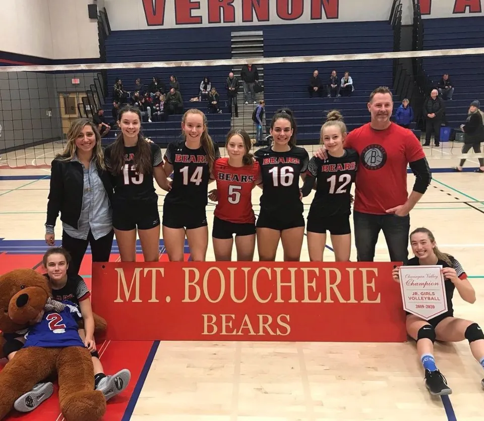 Un gruppo di pallavoliste della Mount Boucherie Secondary School è insieme davanti a uno striscione in palestra.