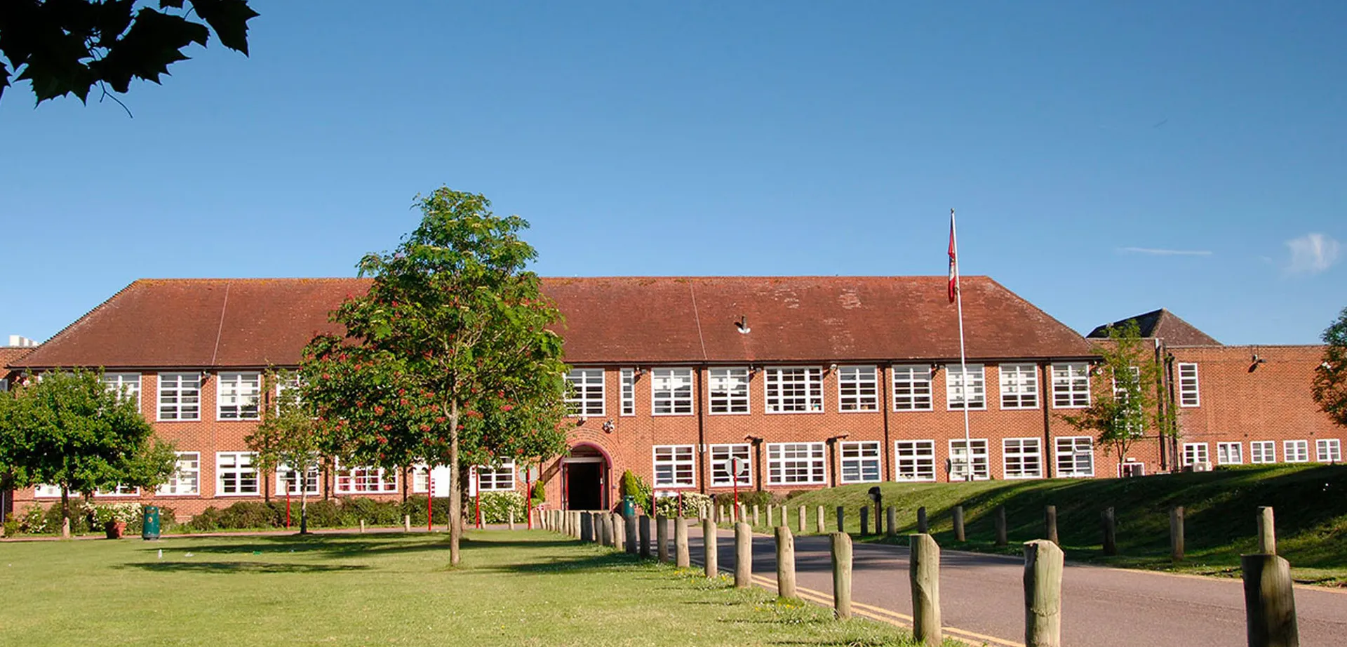 L'edificio in mattoni a più piani con tetto rosso del Brockenhurst College si trova in un'area verde con alberi e cielo blu.