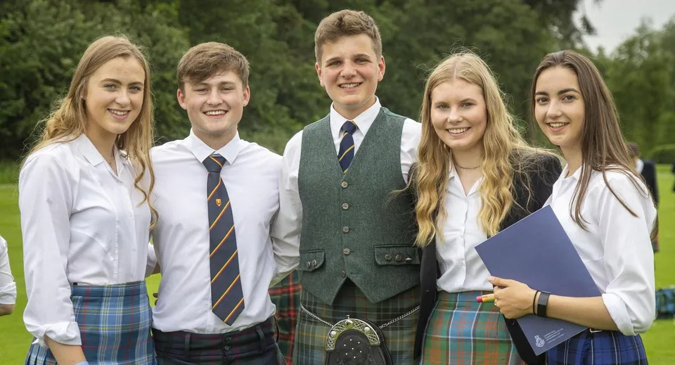 Un gruppo di cinque studenti della Strathallan School si trova insieme all'aperto su un prato con alberi.