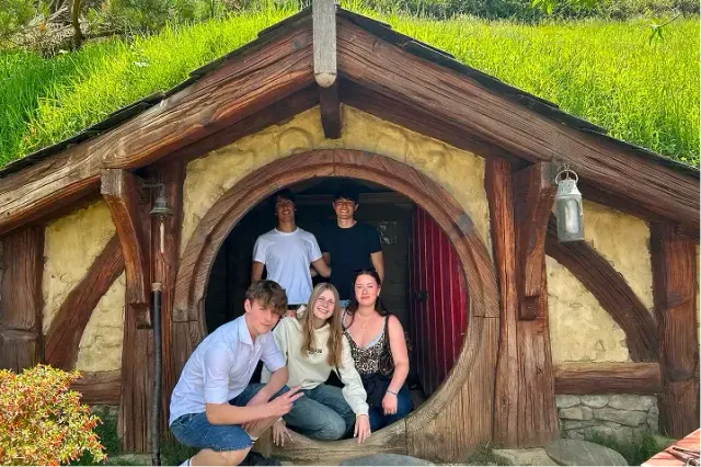 Gruppo di studenti in posa nella porta rotonda di una casa hobbit dal tetto erboso a Hobbiton, Nuova Zelanda