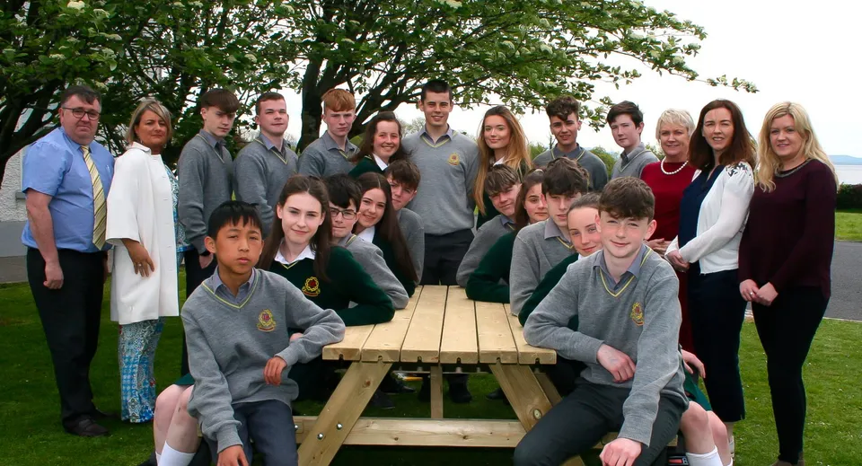 Un gruppo di studenti è seduto attorno a un tavolo di legno all'aperto nel campus della Gortnor Abbey School.