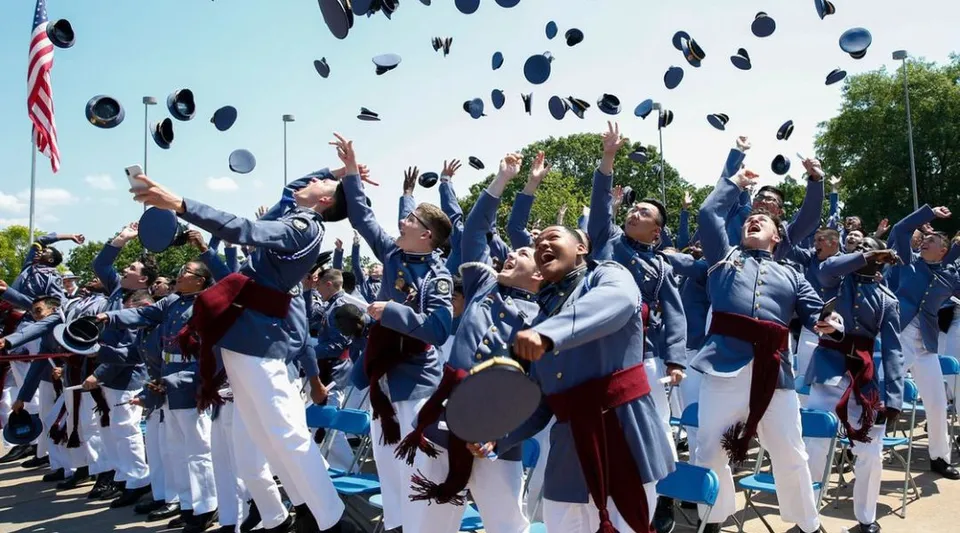 I diplomati della Riverside Military Academy lanciano in aria i loro tocchi davanti a una bandiera americana.