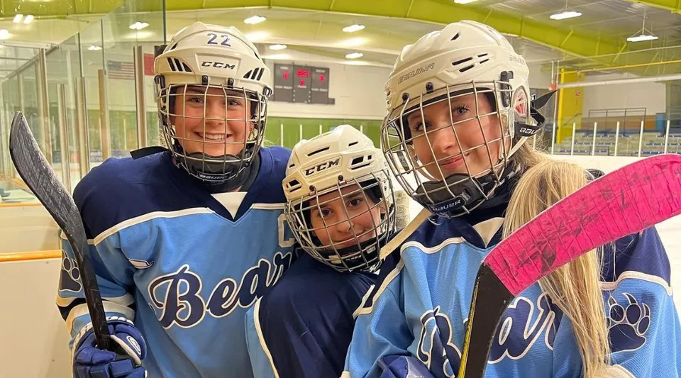 Tre studenti della St. Benedict Catholic Secondary School con l'attrezzatura da hockey su una pista da ghiaccio nella palazzetto del ghiaccio.