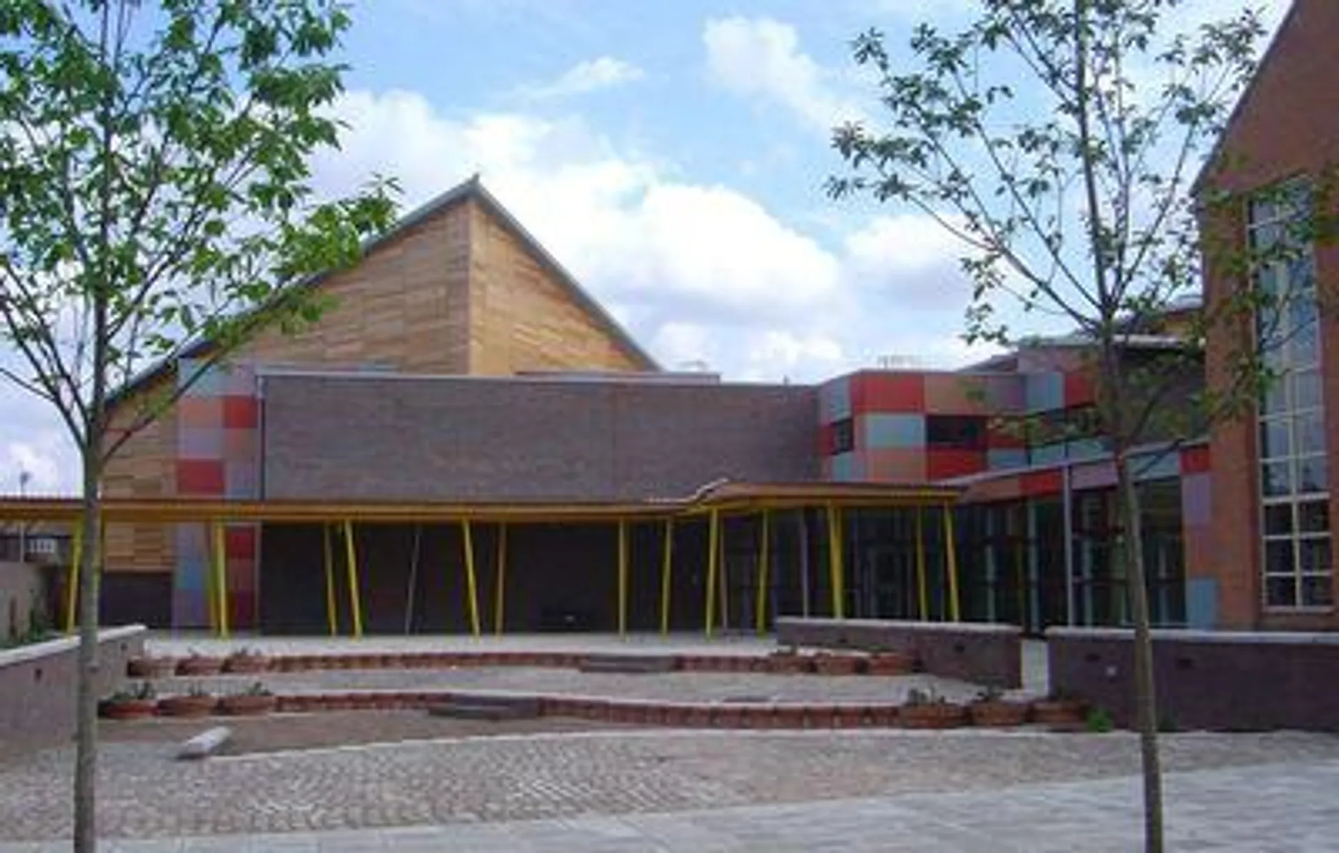 L'edificio moderno con tetto triangolare nel campus della Townley Grammar School è circondato da alberi e da un'area pavimentata.