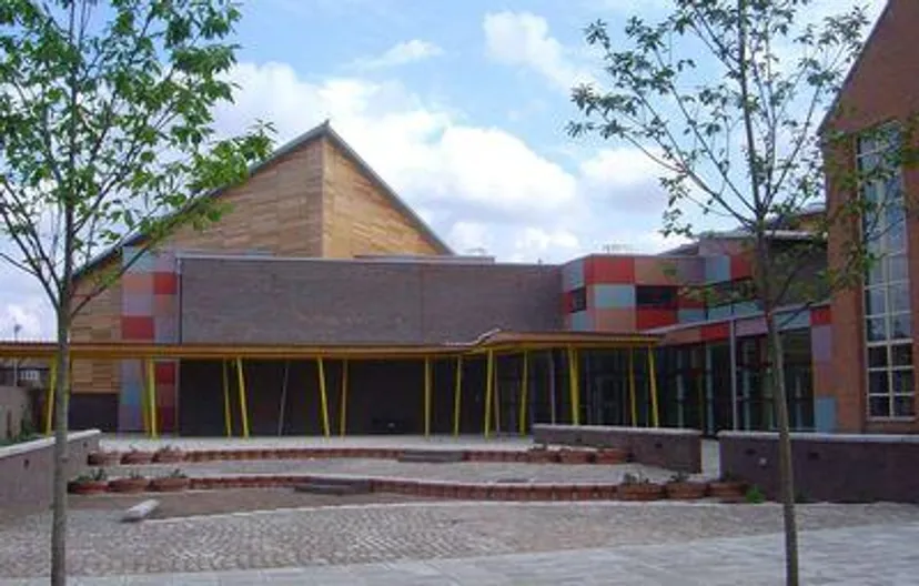 L'edificio moderno con tetto triangolare nel campus della Townley Grammar School è circondato da alberi e da un'area pavimentata.