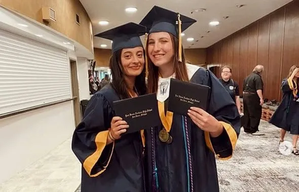 Dos estudiantes sonrientes con birrete y toga de graduación sosteniendo sus diplomas