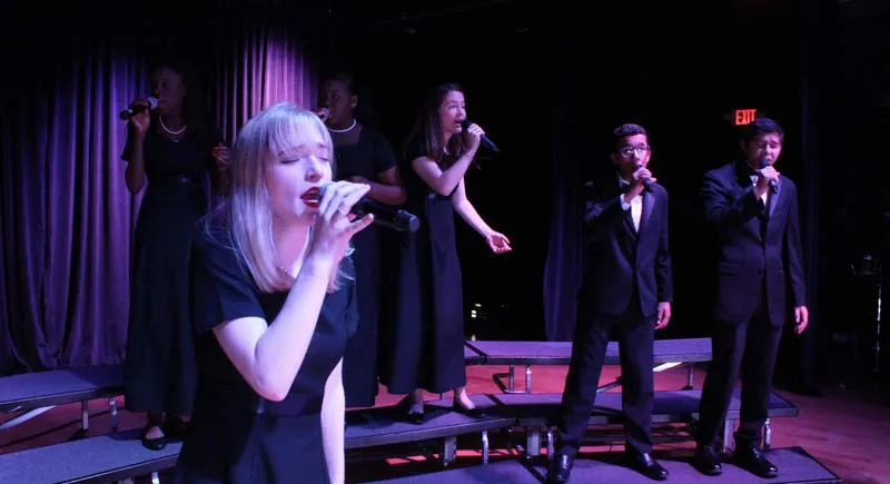 Una mujer con vestido blanco canta en el escenario durante una actuación de la Miami Arts Charter School.