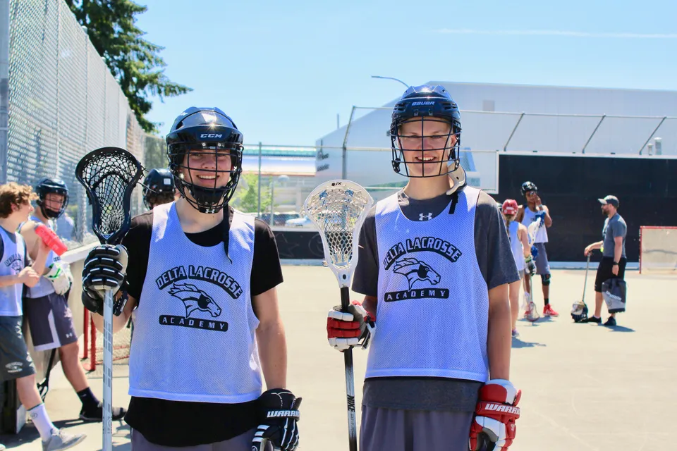 Due studentesse della Delta Secondary School indossano la divisa da lacrosse e si trovano su un campo sportivo.
