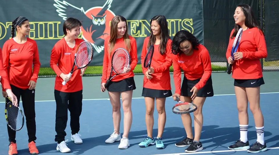 Un gruppo di studentesse in divisa sportiva rossa si trova sul campo da tennis del Foothill College davanti a un grande logo a forma di ala.