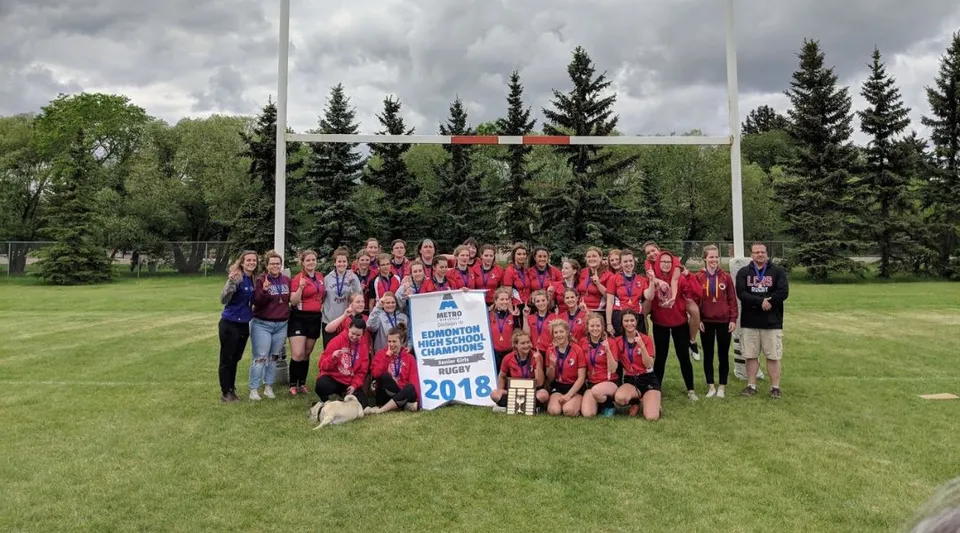 Un grande gruppo di studenti della Leduc Composite High School si raccoglie su un campo da calcio con porta, circondato da pini.