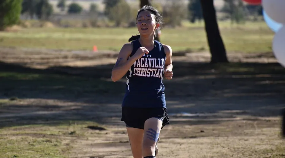 Una studentessa della Vacaville Christian School corre su un sentiero nel bosco circondata da alberi e dal verde.