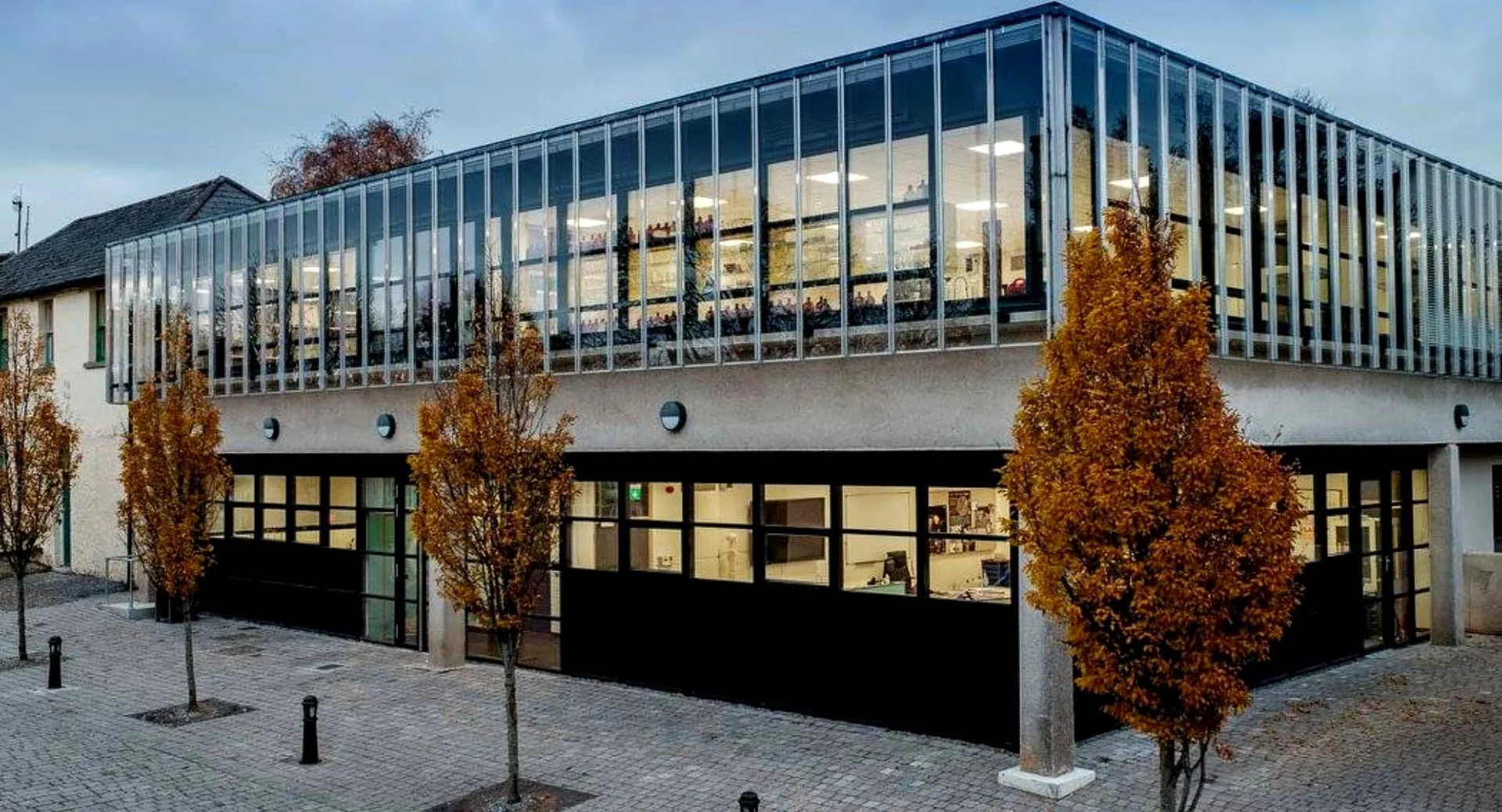 L'edificio moderno del St. Columba's College con un'ampia facciata in vetro e alberi autunnali.