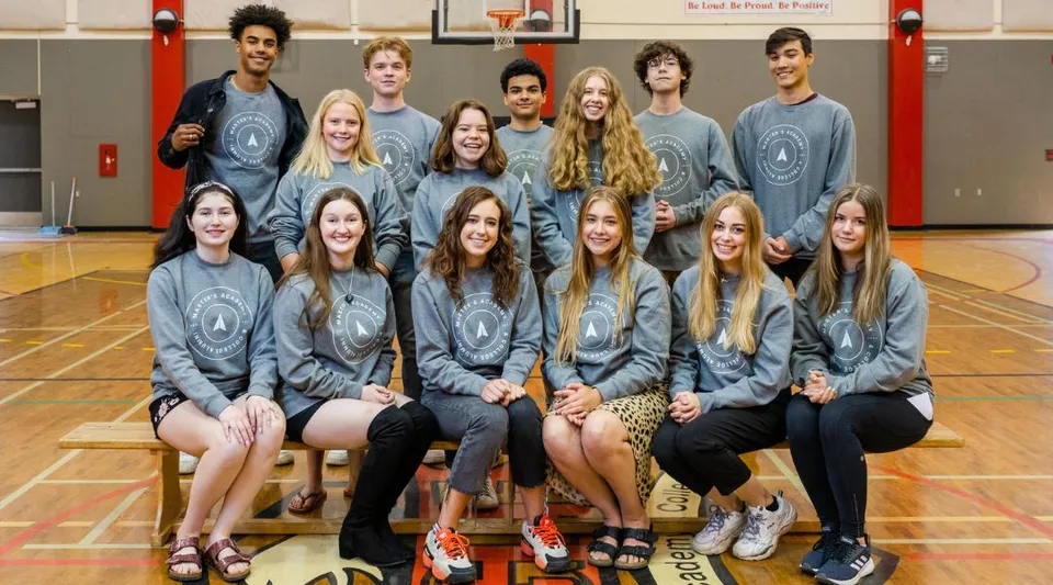 Studenti della Master's Academy and College siedono insieme in palestra e posano per una foto di squadra in divisa scolastica grigia.