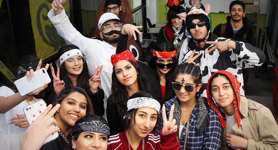 Un gruppo di studenti e studentesse della W.P. Wagner High School posa in diversi costumi davanti a uno sfondo colorato.