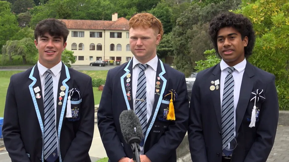 Tre studenti del Nelson College for Boys sono in piedi davanti a un edificio con uno sfondo verde e boscoso.
