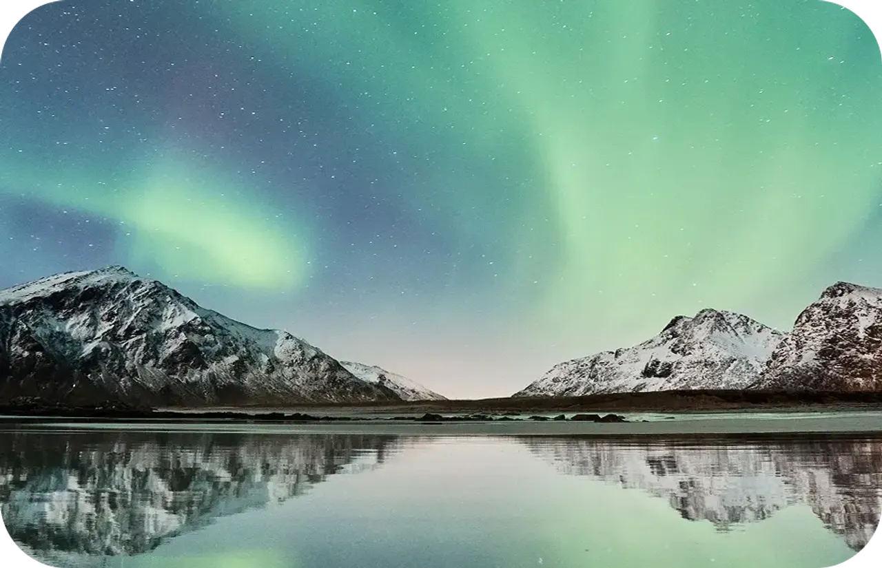 Aurora boreale verde sopra montagne innevate riflesse in un lago norvegese