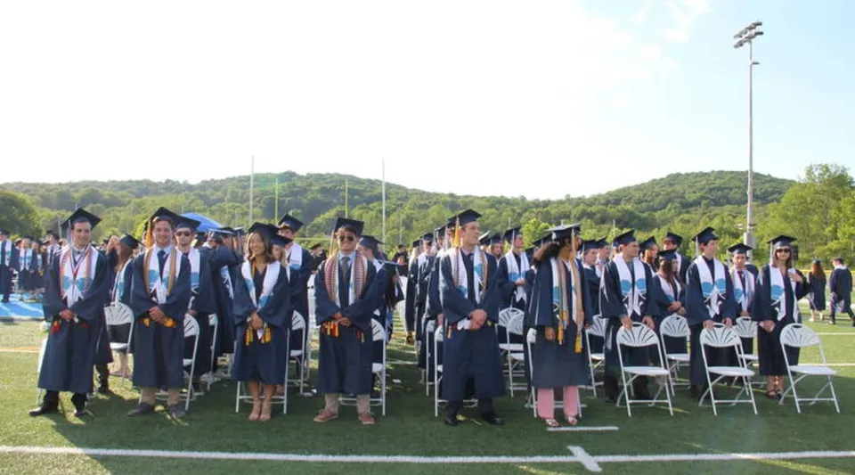 I diplomati della Sparta High School in abito accademico si trovano su un campo con un bosco e un cielo limpido sullo sfondo.
