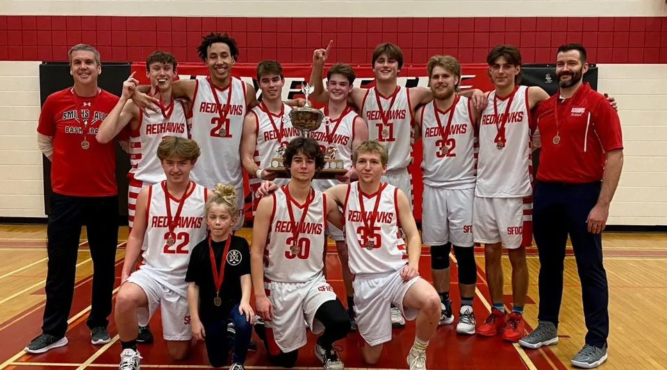 Studenti e studentesse del Smiths Falls District Collegiate Institute posano con un trofeo di pallacanestro nella palestra.